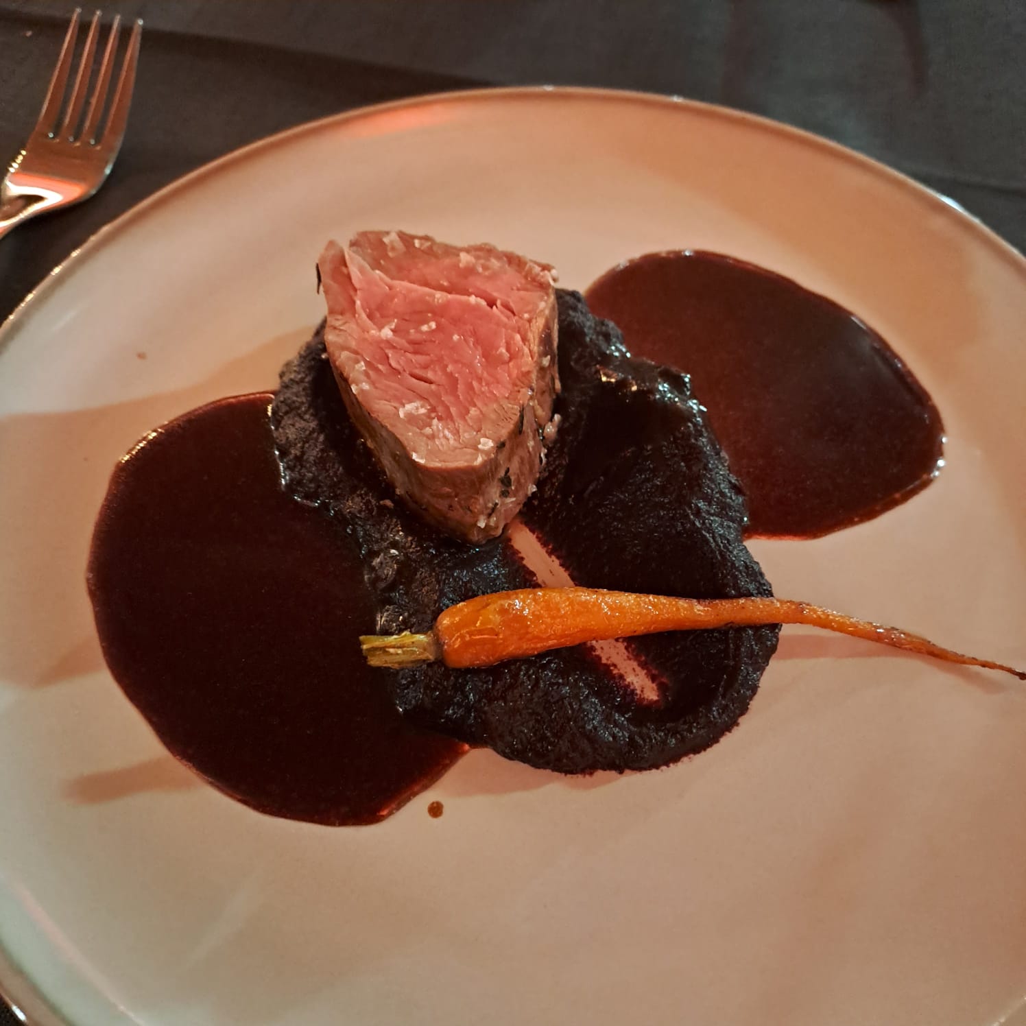 Rinderfilet medium-rare auf Rote-Bete-Püree mit Babykarotte und Jus, präsentiert auf hellem Teller