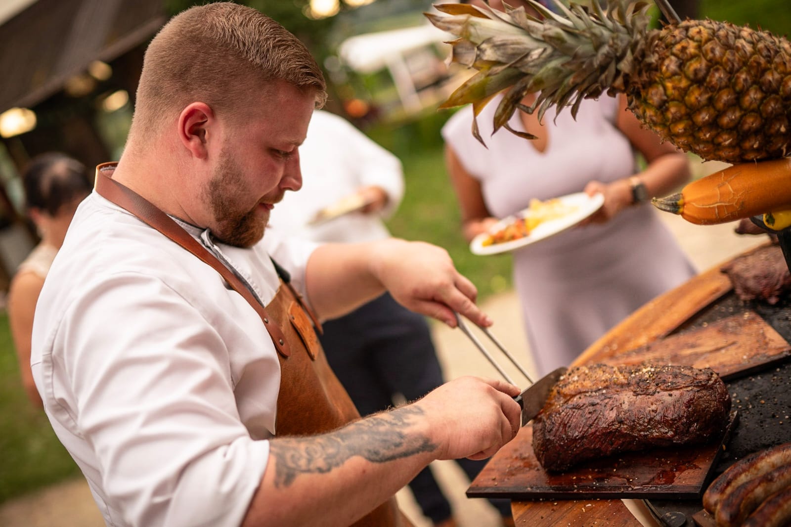 Quirin tranchiert ein Steak am Outdoor-Buffet, im Hintergrund Gäste mit Tellern