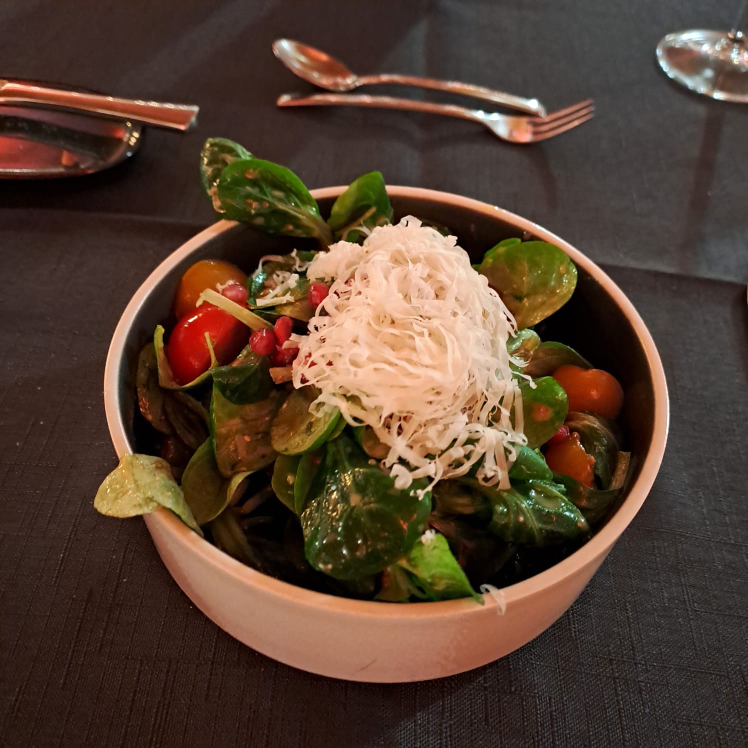 Frischer Feldsalat mit Kirschtomaten, Granatapfelkernen und gehobeltem Hartkäse in dunkler Schale