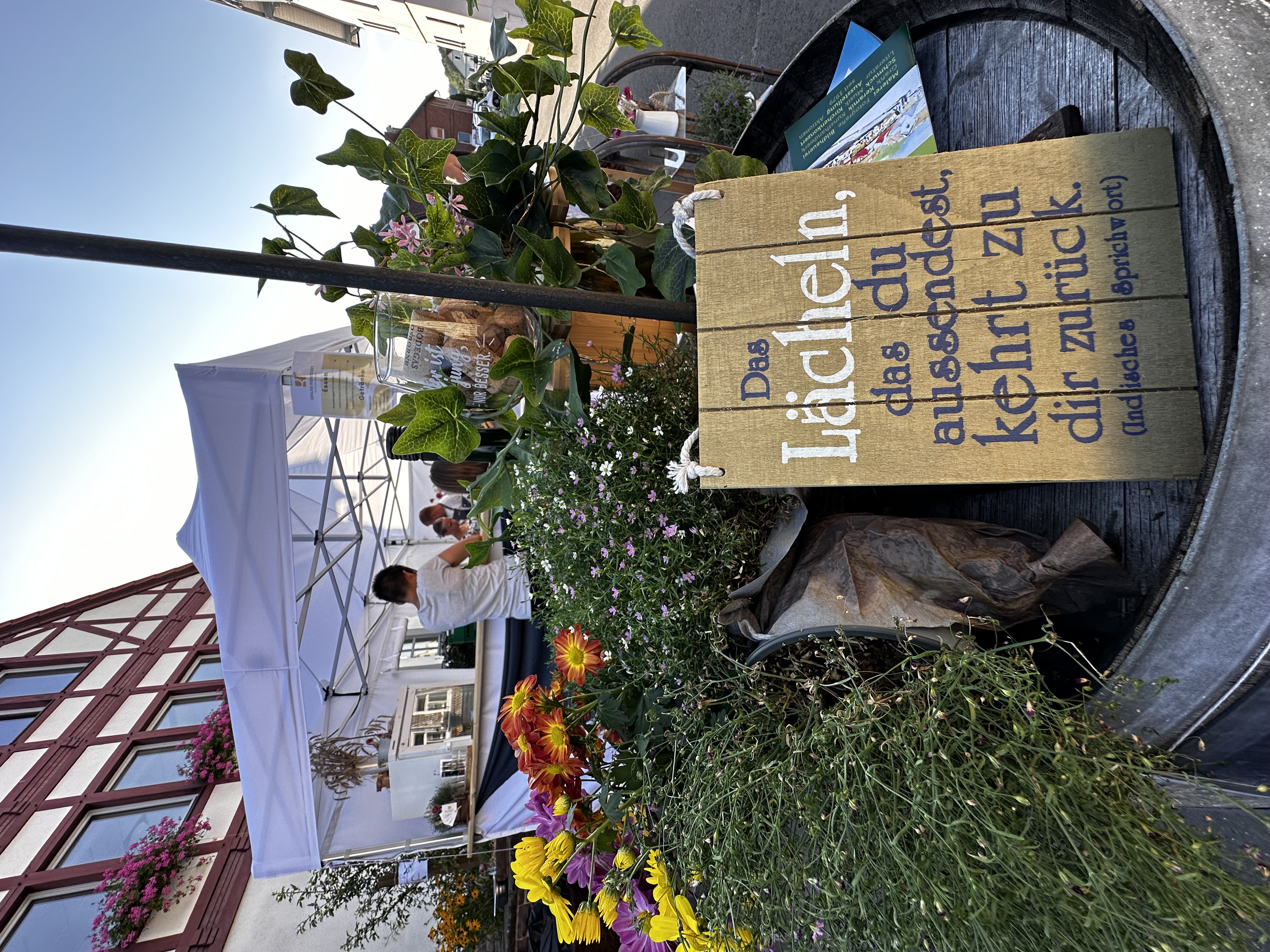 Holz-Schild mit Spruch zwischen Blumen, im Hintergrund das weiße Festzelt