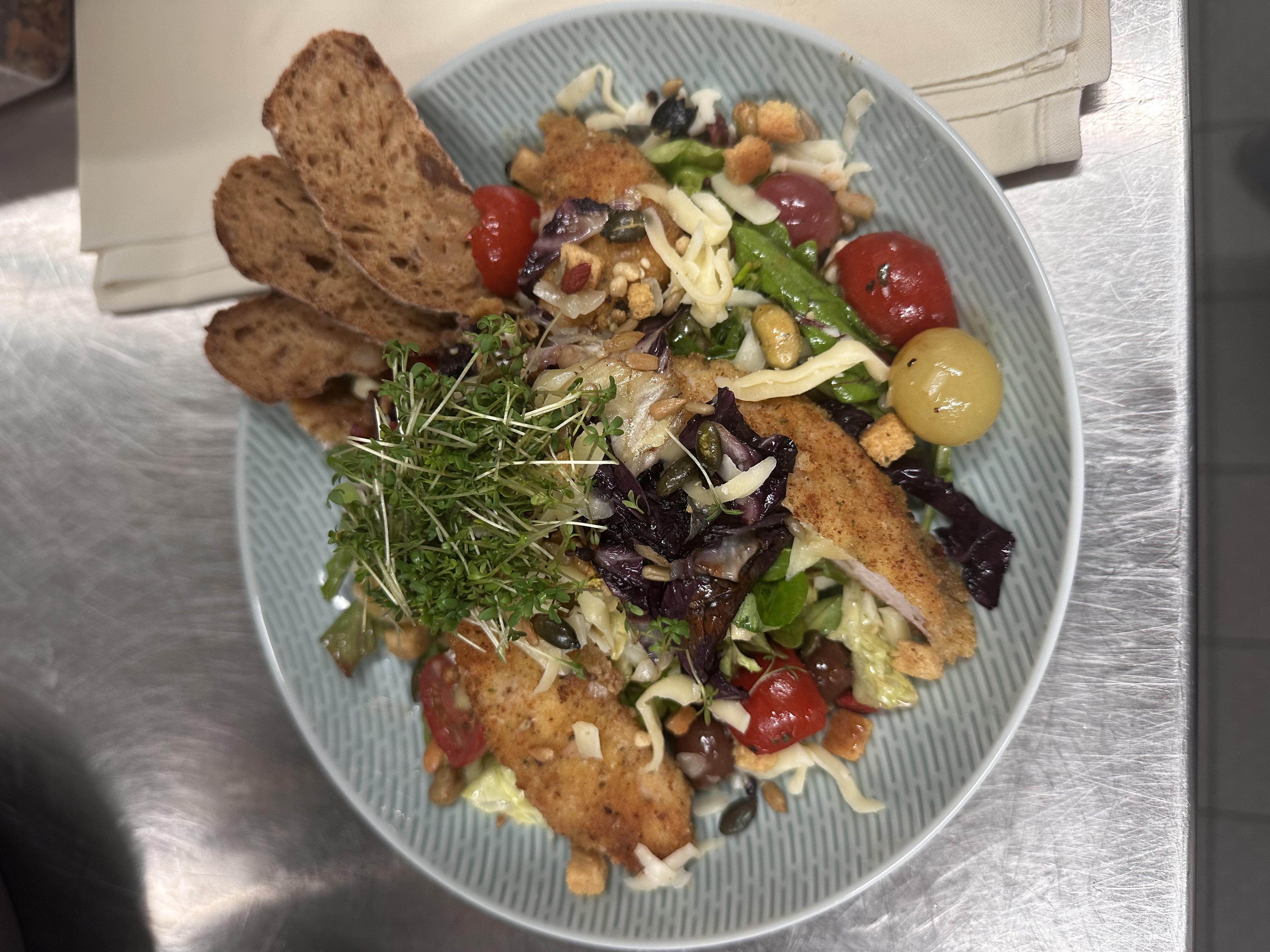 Knusprige Backfisch-Streifen auf gemischtem Salat mit Käsehobel, Kräutern und Brotscheiben