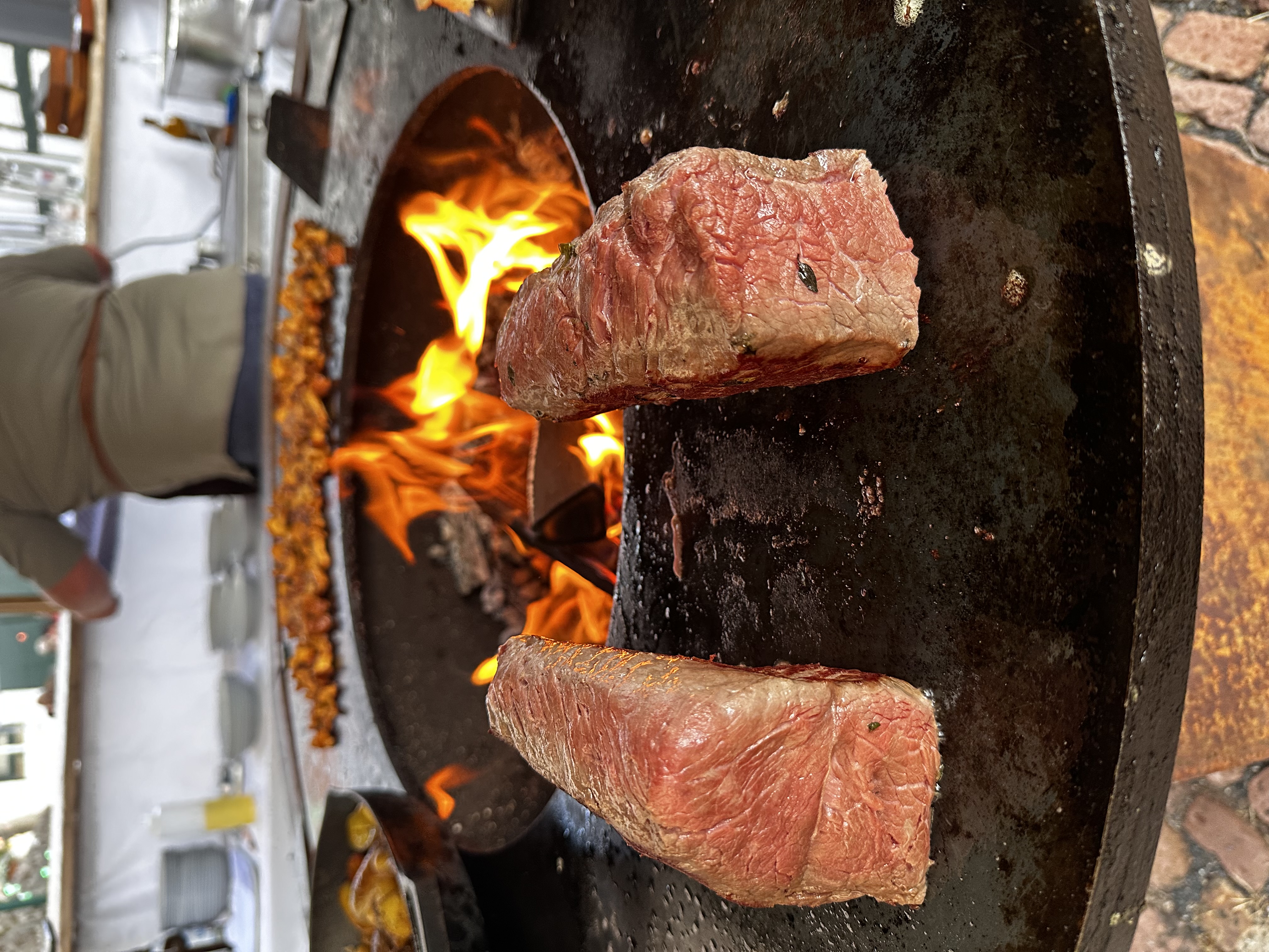 Zwei Steaks auf dem Ofyr-Rost, mit lodernden Flammen im Hintergrund