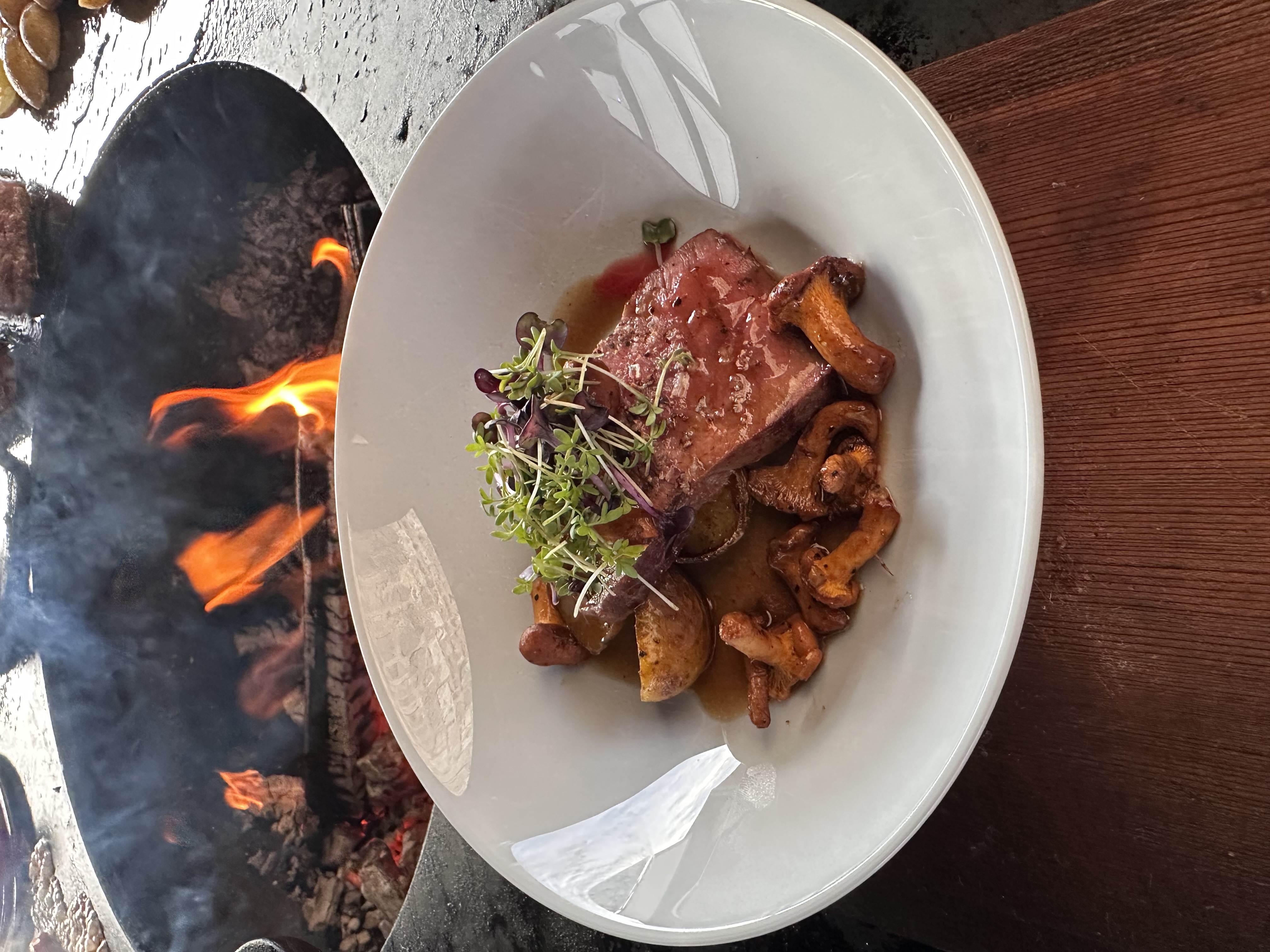 Roastbeef-Scheiben mit gerösteten Pfifferlingen, im Hintergrund das Ofyr-Feuer