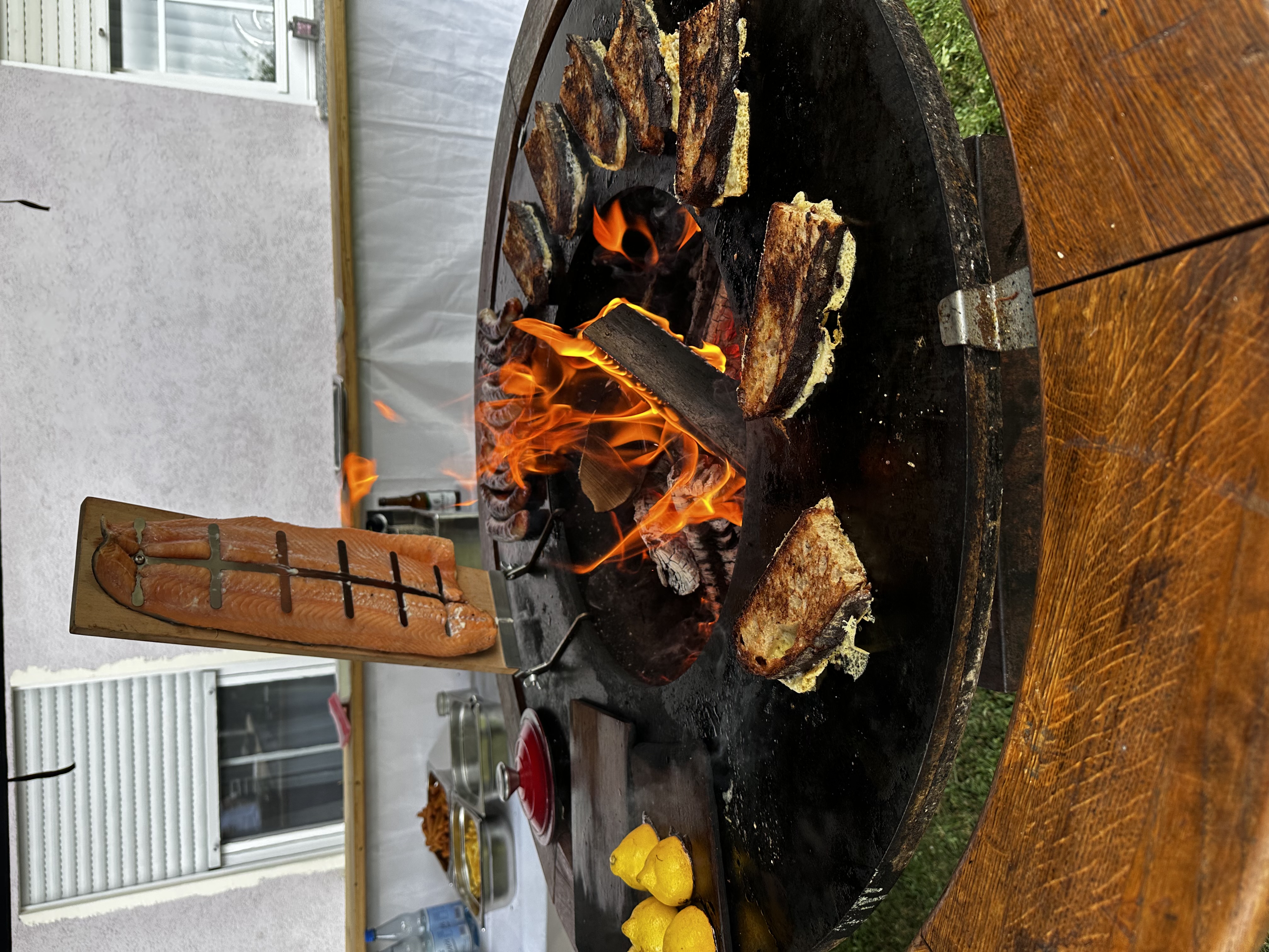 Lachsfilet und Fleischstücke garen auf der Ofyr-Plancha über lodernden Flammen